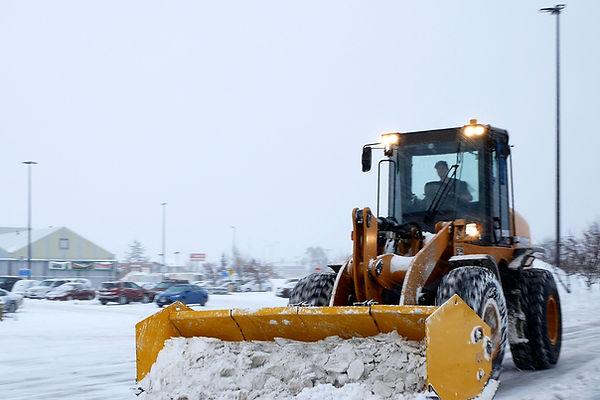 Heavy equipment clearing snow from commercial parking lot